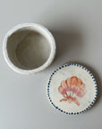 Small ceramic container with a lid featuring a shell design on a wooden surface
