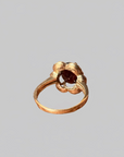 A gold ring with a textured, flower-like top featuring a dark brown central stone, shown against a solid gray background.
