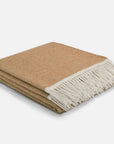 A folded woven throw blanket in a warm tan color with a contrasting off-white fringed edge, shown on a clean light gray background.